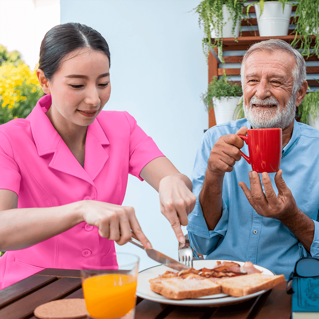 nurse cutting bacon while senior smiles in the background drinking tea