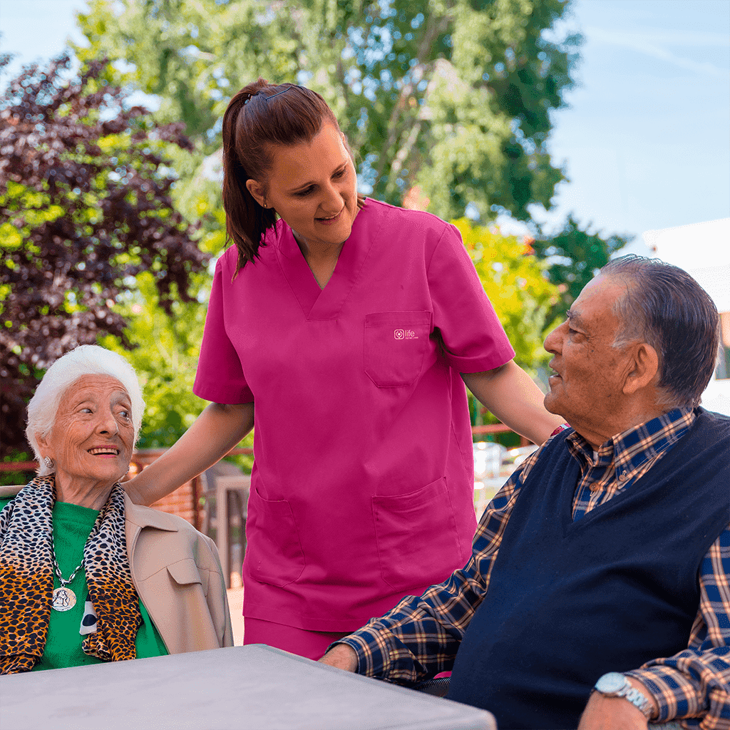 nurse talking to two seniors sitting on a garden