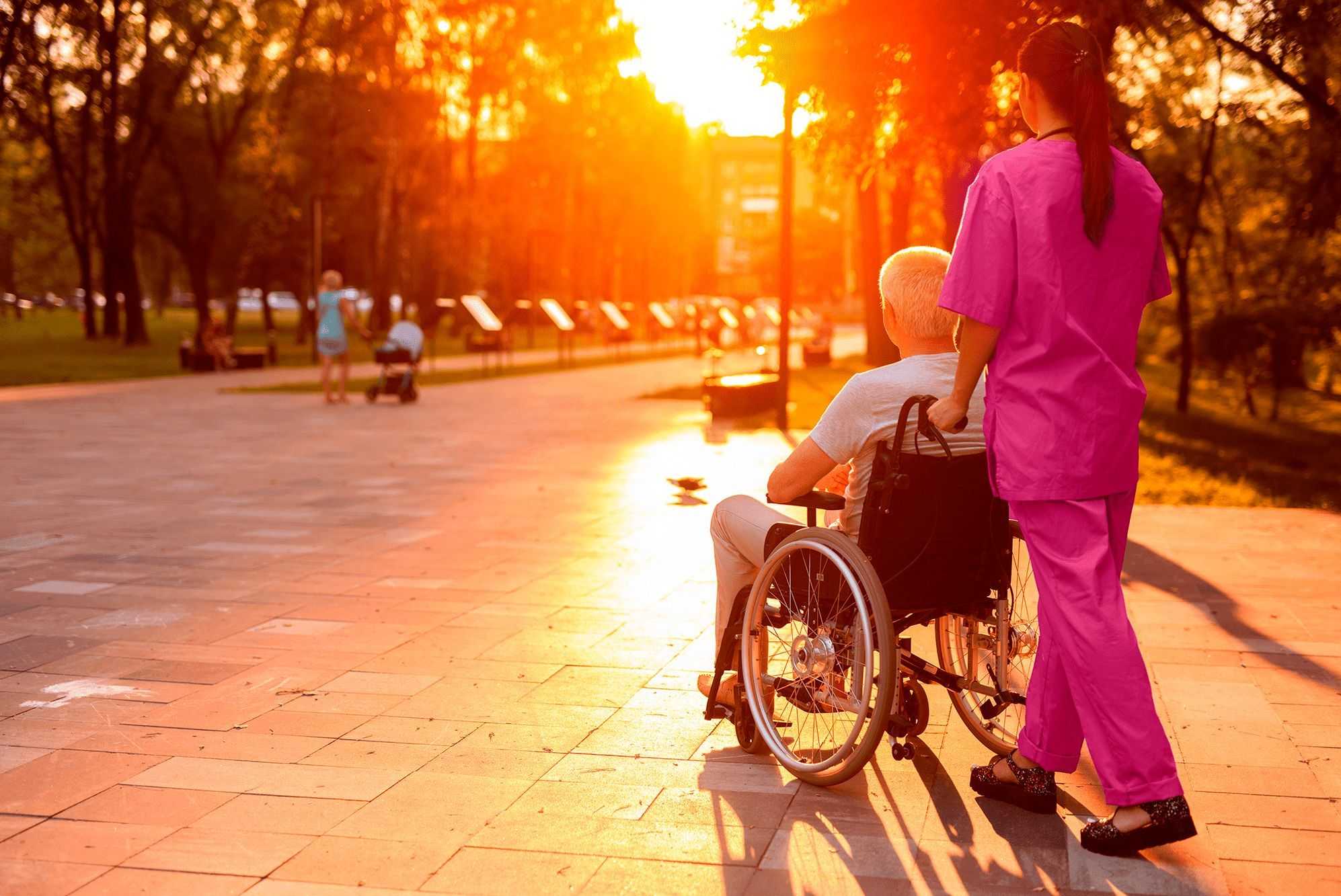 caregiver pushing senior in wheelchair through park