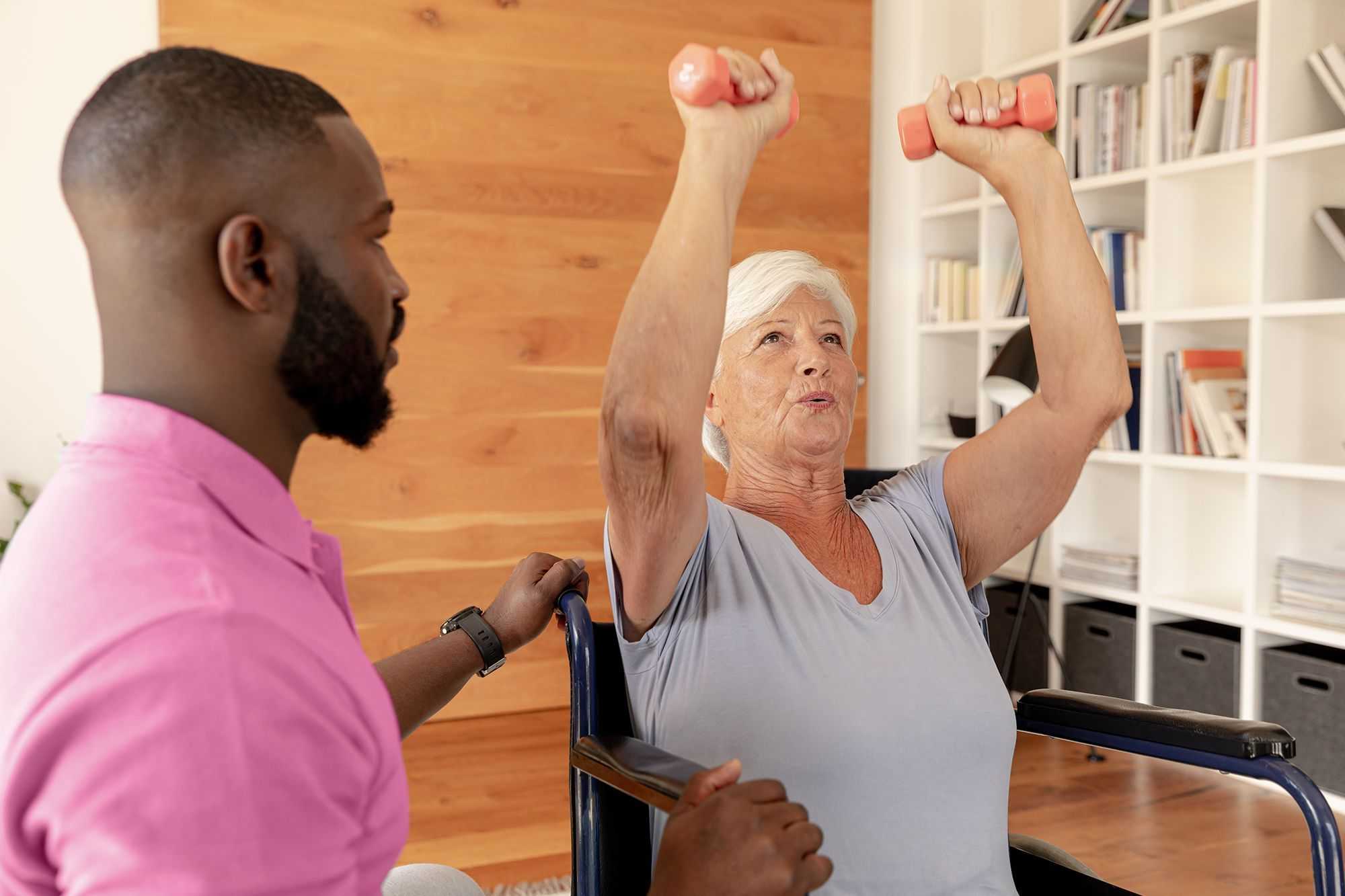 Caregiver watching over senior lady doing  weights