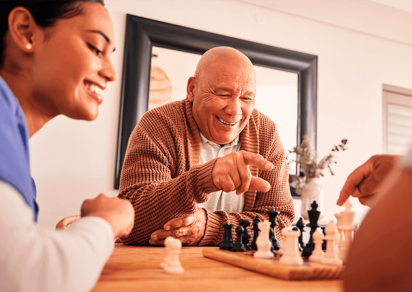 pair of seniors playing chess while caregiver supervises match